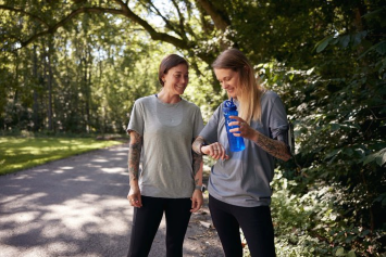 A Veteran stands on a walking trail with a friend and checks their vitals on a smart watch.