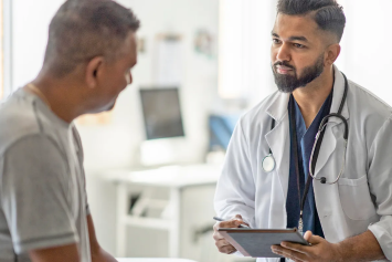 A Veteran sits in a doctor’s office while speaking with a medical professional.