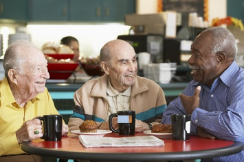 Three Veterans sit at a restaurant table with coffee cups and food in front of them.