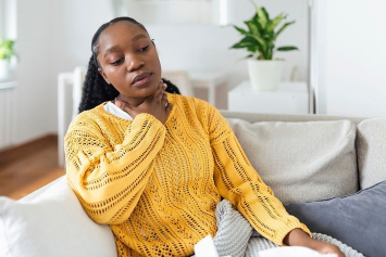 A person sitting down on a couch holds their hand up to their neck.