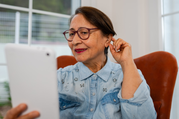 A person holding a tablet checking their hearing aids at home.