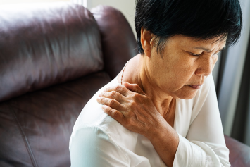 A person grips their shoulder while seated in a chair.