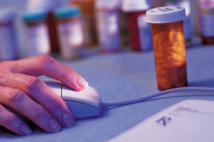 Hand on a computer mouse next to a prescription bottle