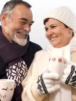 Two people smiling in coats, mittens, holding warm drinks