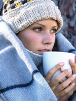 A woman is wrapped in a blanket holding a warm drink