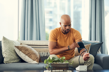 A Veteran checks their blood pressure at home in their living room.