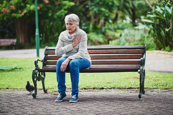 A Veteran sitting on a park bench, holding a hand against her chest