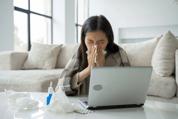 A Veteran sneezing into a tissue in her living room at her laptop