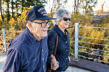 A Veteran and their partner holding hands, walking along a wooded trail